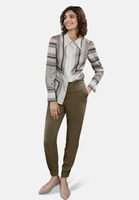 Gelaagde blouse met patronen in geometrische ontwerpen in wit, marineblauw en bruin; gecombineerd met olijfgroene tapered broek; lichtbeige hakken.