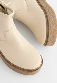 Beige Leder-Stiefeletten mit glatter Oberfläche, runden Zehen und einer dicken, strukturierten beige-sohle mit braunen Akzenten.