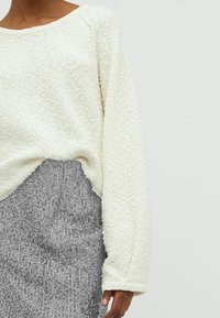 Pull crème riche en texture avec une coupe ample et un col large, associé à une jupe pailletée argent métallique avec des rayures verticales.