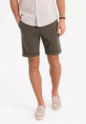 Grønne stofshorts med optrukne sømme, der har en struktureret overflade. Parret med en lys farvet skjorte med knapper og beige slip-on sko.