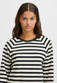 Striped long-sleeve top in black and white, featuring a round neckline and raglan sleeves, made of a smooth, lightweight fabric.