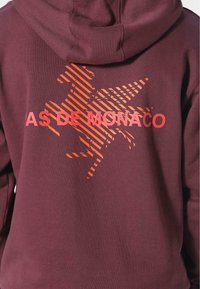 Felpa bordeaux con una grande grafica arancione di un cavallo e il testo "AS DE MONACO" in lettere rosse in grassetto. Materiale in cotone morbido.