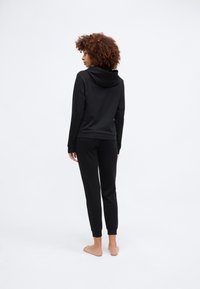 Black sweatshirt with a hood, paired with fitted pants, both made from soft fabric. The design features ribbed cuffs and a minimalist style.