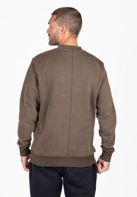 Brązowy sweatshirt z okrągłym dekoltem, ściągaczami przy mankietach i brzegu oraz pionowym szwem na plecach. Miękki materiał i luźny krój.
