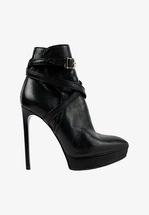 Bottine noire à talon haut avec bout pointu, semelle plateforme, brides enroulantes et détail de boucle argentée sur cuir lisse.