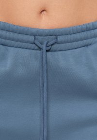 Φωτεινή γαλάζια ζώνη με κορδόνι, κατασκευασμένη από απαλό ύφασμα, με πλεκτό δέσιμο και λεία υφή, με ελαφριά γυαλάδα.