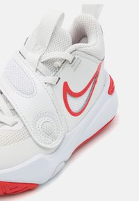 Białe sneakersy Nike z siateczkową cholewką, czerwonymi akcentami, wyściełanym kołnierzem oraz teksturowanym paskiem z okrągłym detalem z boku.