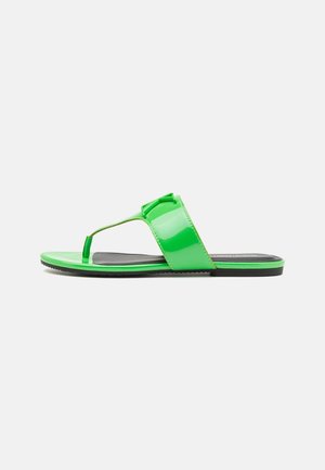 Sandale plate en cuir verni vert avec entre-doigt et large bride sur le dessus du pied, vue de profil sur un fond uni.