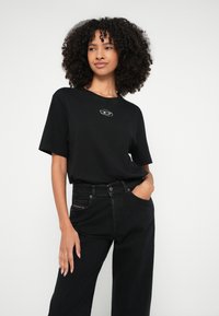 Tricou negru din bumbac cu mâneci scurte, având un logo argintiu pe piept. Asortat cu blugi negri cu talie înaltă. Textură netedă.