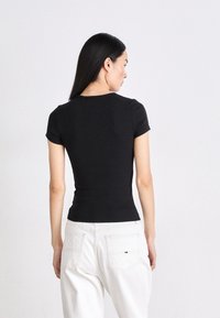 T-shirt nera aderente con maniche corte e scollo rotondo, abbinata a pantaloni bianchi a vita alta, che mostrano una texture di tessuto liscia.