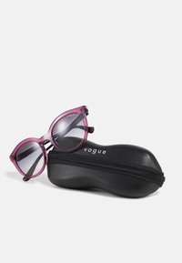 Ochelari de soare translucizi lila cu lentile gradient, așezați pe un toc negru cu fermoar, având brandul "vogue" scris cu text alb.