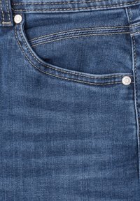 Zbliżenie na przednią kieszeń niebieskich jeansów z widocznym przeszyciem i metalowymi nitami.