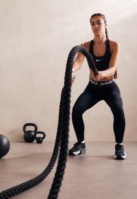 Black fitness apparel, including a cropped top and high-waisted leggings, with a braided rope in motion against a neutral background.