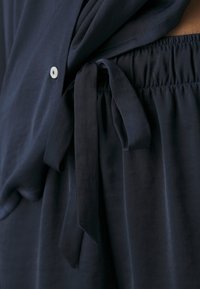 Marinblå tvådelad outfit med en lös topp med detaljer i form av knappar och byxor med resårmidja och en knytning i satin. Mjuk textur.