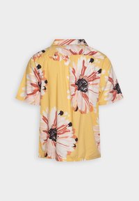 Korte mouwen shirt met een gele achtergrond en grote witte en roze bloemenpatronen. Gemaakt van lichtgewicht stof.