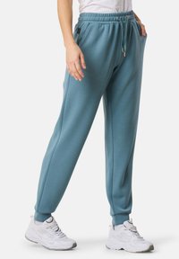 Hellblaue Sweatpants mit elastischem Bund und Kordelzug, ausgestattet mit Seitentaschen und schmal zulaufenden Bündchen. Kombiniert mit weißen Sportschuhen.