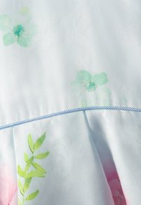 Hellblauer Stoff mit dezenten Blumenmustern in Grün und Rosa. Verfügt über ein gerafftes Design und ist an der Naht mit einem blauen Rand akzentuiert.