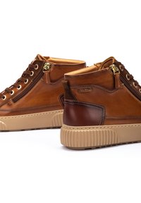 Des chaussures montantes en cuir marron avec une semelle plateforme texturée beige. Elles présentent des accessoires en or, une fermeture éclair sur le côté et un accent marron sur le talon.