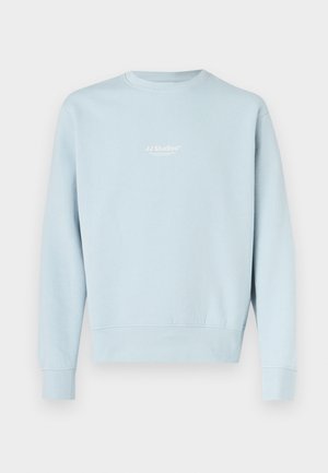 Sweat-shirt bleu clair avec poignets et ourlet côtelés, arborant un petit logo blanc "JJ Studios" sur le devant. Tissu doux, design décontracté.