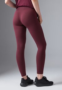 Leggings căptușite în nuanța vișinie, cu o talie înaltă, asortate cu pantofi sport negri. Materialul pare elastic și aderent.