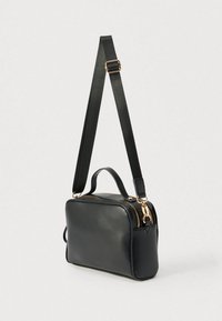Czarna skórzana torba na ramię z odpinanym paskiem, podwójnymi zamkami błyskawicznymi i małym górnym uchwytem. Charakteryzuje się gładką fakturą i złotymi elementami ozdobnymi.