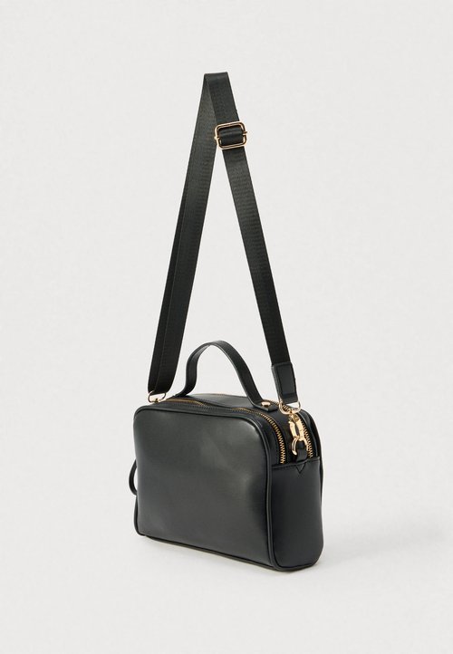 Schwarze Leder-Umhängetasche mit abnehmbarem Riemen, zwei Reißverschlüssen und kleinem Tragegriff oben. Sie hat eine glatte Oberfläche und goldfarbene Metalldetails.
