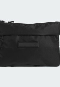 Bustina nera con zip realizzata in tessuto strutturato. Presenta una forma piatta, un design lineare e un patch con logo in gomma brandizzato sul davanti.