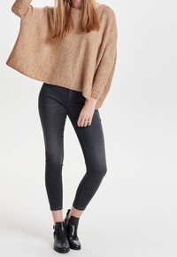 Béžový, texturovaný oversized svetr s žebrovanými rukávy, kombinovaný s černými slim kalhotami a kotníkovými botami, tvořící neformální outfit.