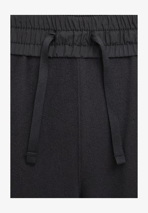 Zwarte fleece joggers met een elastische tailleband met een geraffineerde afwerking en een zwart trekkoord. Zachte textuur met zichtbare stikseldetails.