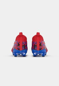 Des crampons de football rouges et bleus présentent une tige texturée et un design graphique, avec une languette au talon et des pointes moulées pour une meilleure traction.