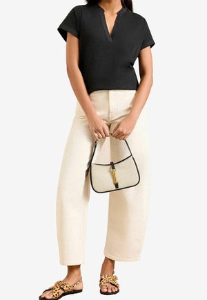 Schwarzes Kurzarmoberteil mit V-Ausschnitt, cremefarbene Hosen mit weitem Bein und Sandalen mit Leopardenmuster. Hält eine kleine beige Handtasche mit schwarzen Akzenten.