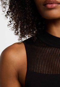 Haut sans manches noir avec un col montant côtelé et des panneaux rayés transparents, mettant en valeur la texture et le design au niveau de la partie supérieure des épaules.