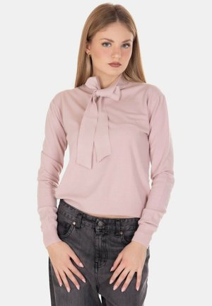 Maglia a manica lunga rosa chiaro con dettagli a fiocco al collo, realizzata in tessuto morbido, abbinata a jeans grigi scuri a vita alta.