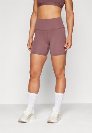 Bordeaux high-waisted sportshorts met een gladde textuur, gecombineerd met witte sportsokken en lichte sneakers, staand op een neutrale achtergrond.