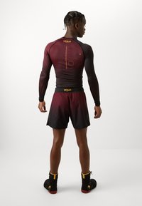 Μακρυμάνικο μαρούλι και μαύρο rash guard με κίτρινες λεπτομέρειες και γεωμετρικά μοτίβα σε συνδυασμό με μαρούλι σορτς που διαθέτει λογότυπο στη ζώνη.