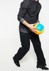 Felpa con cappuccio grigia scura con zip, pantaloni sportivi neri, mentre tiene una palla da volleyball colorata (blu, gialla, arancione) in una posa dinamica.