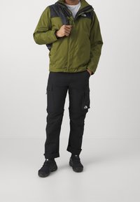 Grøn og sort jakke med lynlås, parret med sorte cargo-bukser med sidelommer og manchetter. Sorte vandrestøvler fuldender outfittet.