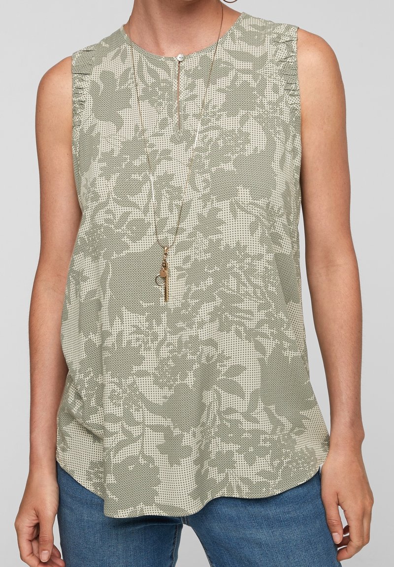 Blouse sans manches vert clair à motif floral, avec un col rond et des plis subtils aux épaules. Associée à un denim.