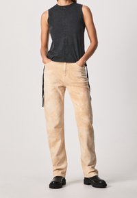 Svart ärmlös topp, beige högmidjade byxor med sidoknytningar och svarta kraftiga plattformskängor; släta texturer och minimalistisk design.