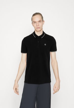 Polo negro con cuello con ribete blanco y tapeta de tres botones. Incluye un pequeño logotipo en el lado izquierdo del pecho. Tejido suave.