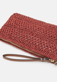 Borsa a mano intrecciata rossa con superficie testurizzata, cerniera dorata e un manico a polso marrone per una facile portabilità. Design compatto per gli essenziali.