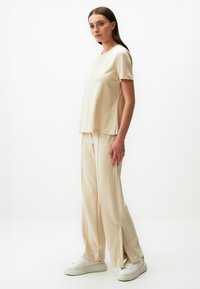 Beżowa bluzka z krótkim rękawem i okrągłym dekoltem, zestawiona z szerokimi spodniami z bocznymi rozcięciami, uzupełniona białymi trampkami.