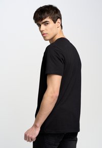 Camiseta negra de manga corta y cuello redondo en algodón, con dobladillo recto y ajuste relajado, modelada por un joven visto de perfil.