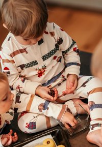 Pyjamaha z dolgimi rokavi v kremni barvi z živahnimi vzorci živali in daril. Mehka tkanina, gumb v ovratniku in sproščen kroj s kontrastnimi črtami.