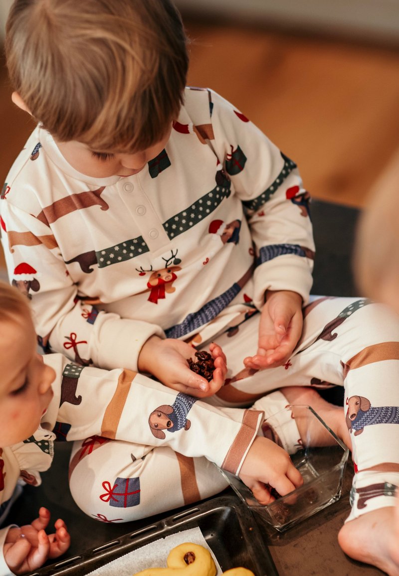 Pyjamaha z dolgimi rokavi v kremni barvi z živahnimi vzorci živali in daril. Mehka tkanina, gumb v ovratniku in sproščen kroj s kontrastnimi črtami.