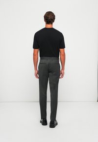 Zwart kortom shirt gecombineerd met grijze, slim-fit dress pants met een subtiele textuur, twee achterzakken en zwarte nette schoenen.