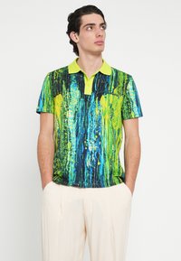 Rövid ujjú galléros póló élénk zöld és kék absztrakt mintával, világos sárga gallérral és kényelmes szabással.