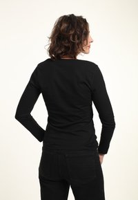 Schwarzes Langarmshirt mit Rundhalsausschnitt, aus einem glatten Stoff, kombiniert mit dunklen Jeans; schlichtes Design, keine sichtbaren Muster oder Beschläge.