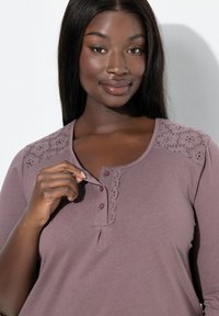 Top a maniche corte di colore malva, con pizzo occhiellato decorativo sulle spalle, patta con bottoni e scollatura tonda. Texture in cotone morbido.