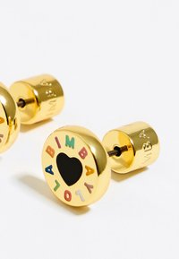 Pendientes de studs en color dorado que presentan un diseño redondo con un corazón negro en el centro y letras coloridas que deletrean "ABIMBA" alrededor del borde.